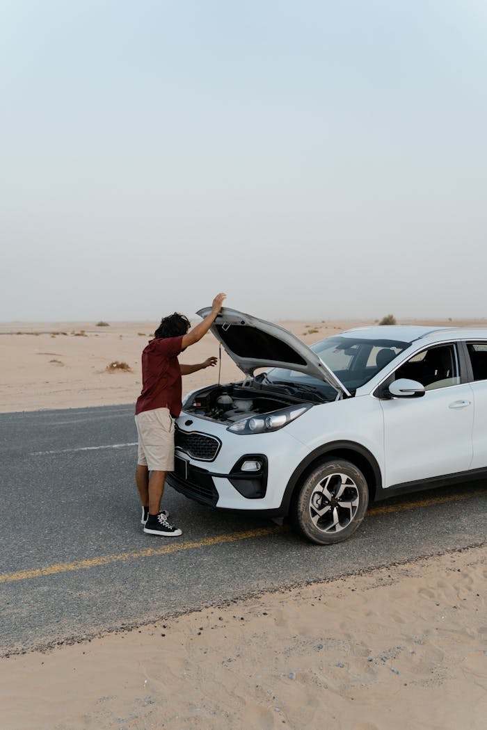 services-01 A man inspecting the engine of a car by the roadside in a desert setting.